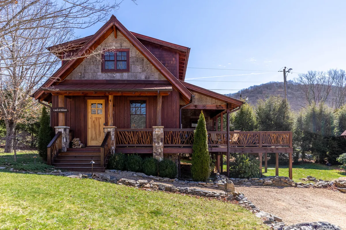 This image captures the inviting exterior of the cabin, with a wooden front door, stone accents, decorative railings, and lush greenery surrounding the entrance. The space suggests a welcoming transition from outdoor adventure to home base, with a cozy porch area perfect for both guests and their furry companions to relax after a day exploring.