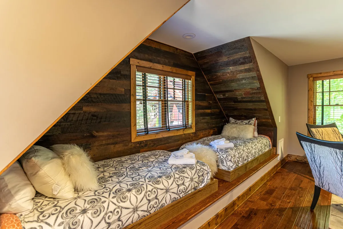 Two twin beds nestled in a wood-paneled alcove, with a large window offering natural light and greenery views. The beds are positioned for both privacy and togetherness, with simple, comfortable bedding, making the space ideal for children or friends.
