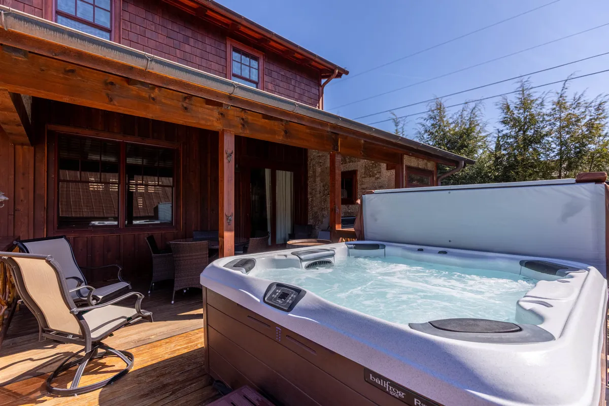 An exterior shot of the cabin's wooden deck, featuring a private jacuzzi surrounded by lush greenery. The hot tub is the focal point, inviting relaxation in a peaceful, natural setting—ideal for stargazing or unwinding outdoors as a couple.