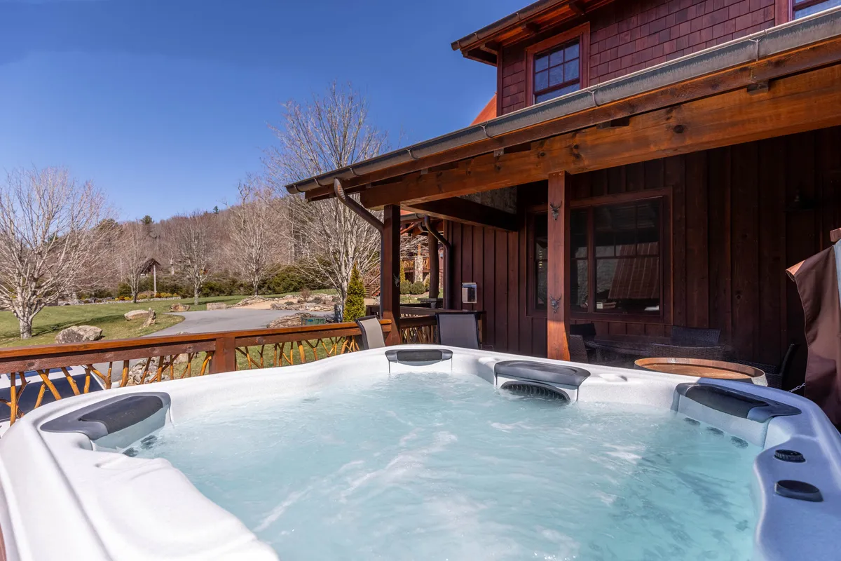 An inviting outdoor space featuring a hot tub on a wooden deck surrounded by trees. The peaceful setting emphasizes relaxation in nature, with the hot tub visible and ready for use, suggesting both social and solitary enjoyment.