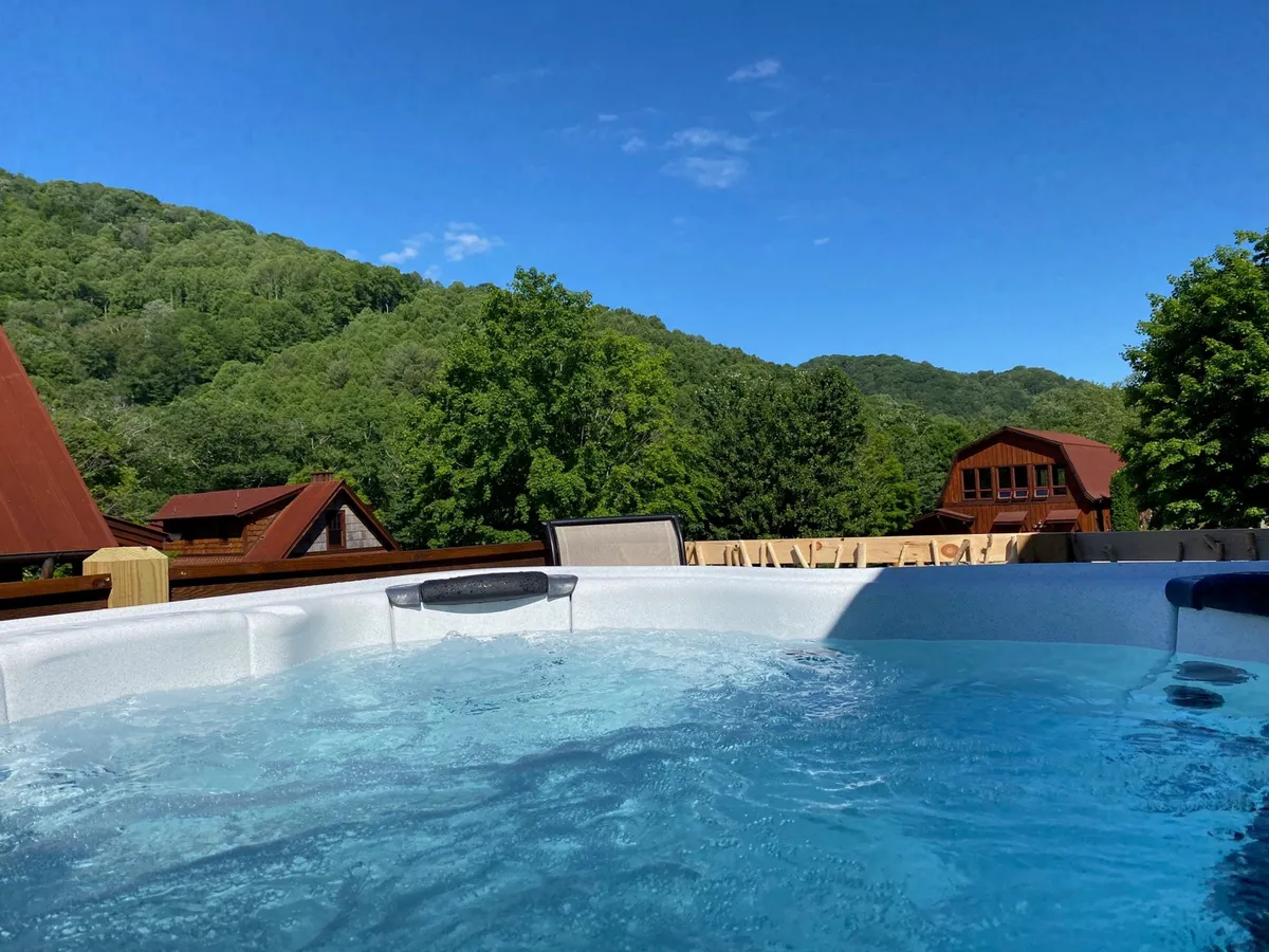 A scenic outdoor view with a hot tub overlooking mountain vistas and neighboring wooden cabins. The setting is tranquil, perfect for soaking while enjoying expansive natural views at sunset or under the stars.