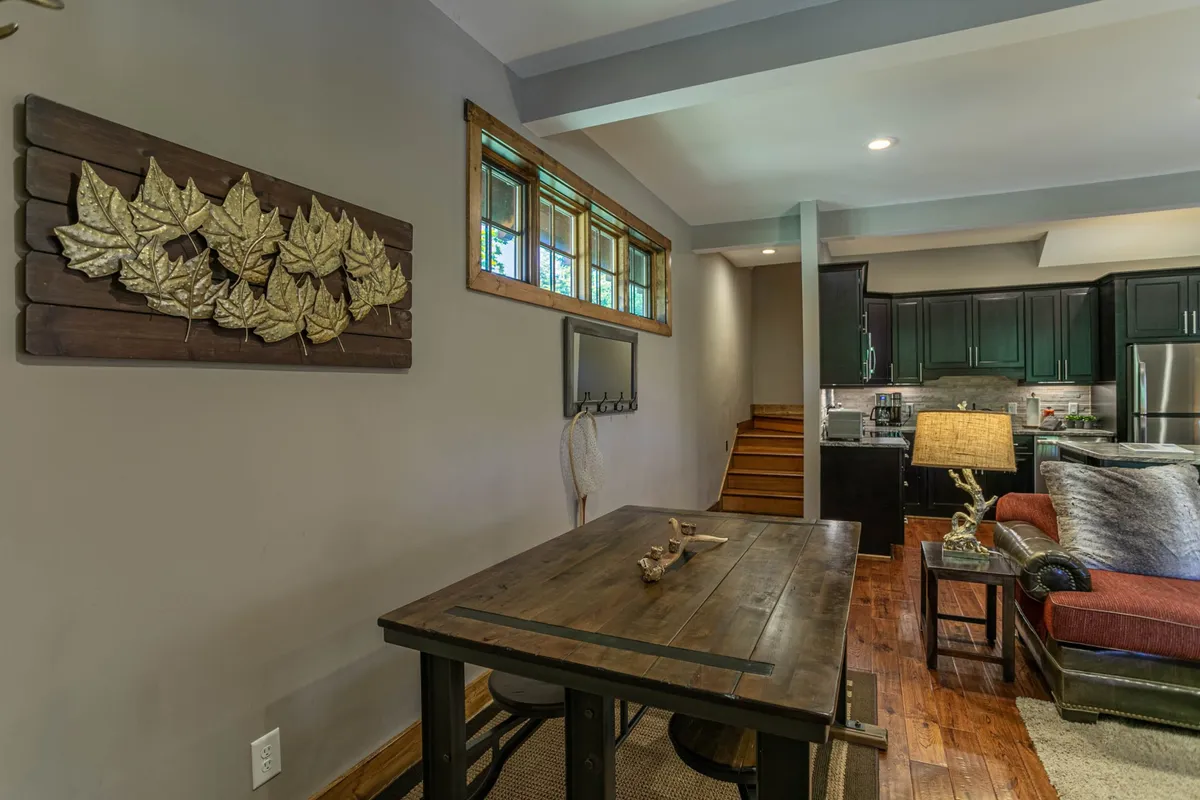 A cozy dining area with a table set for four, adjacent to the kitchen and a sitting area, with soft lighting and decorative wall art providing an inviting ambiance. The open-concept design is evident, seamlessly connecting eating, dining, and relaxing spaces.
