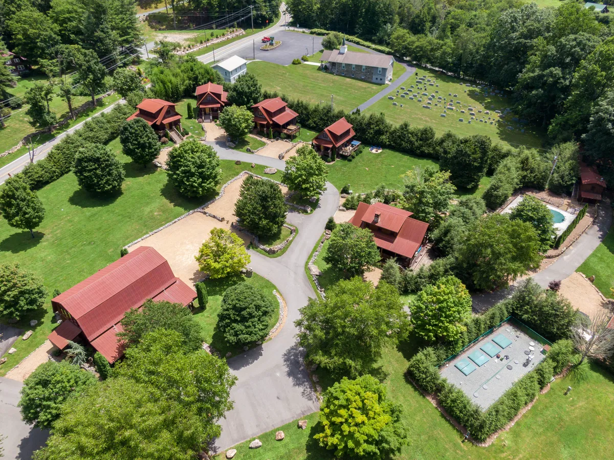 A wide exterior view showcases several red-roofed cabins nestled among landscaped gardens, with a central swimming pool and meandering walking paths. The scene is vibrant and inviting, offering a glimpse of communal outdoor spaces ideal for family gatherings, swimming, and relaxation amidst nature.