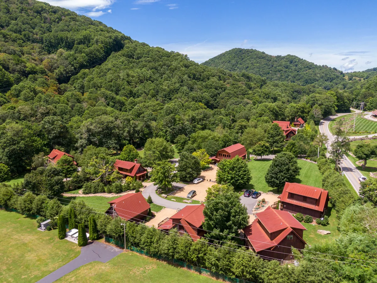 An inviting aerial perspective reveals red-roofed cabins set against lush greenery and surrounding mountains, with a winding driveway leading through the property. The expansive natural landscape encourages exploration and outdoor recreation, evoking a sense of adventure and connection to the mountains.