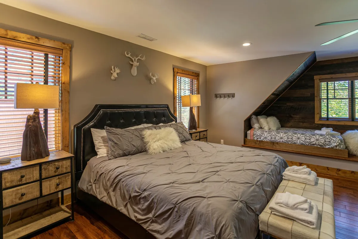 A king-sized bed with plush bedding and warm lighting, accented by natural wooden elements. The space feels inviting and spacious—ideal for families or groups, with enough room for additional sleeping arrangements not fully visible in frame. The overall ambiance is cozy and restful.