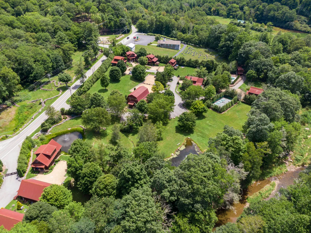 A cluster of inviting cabins by a tranquil pond, bordered by a tree line and open green space. A small road hints at easy access to nature, and the open landscape invites activities like hiking, fishing, and family gatherings.